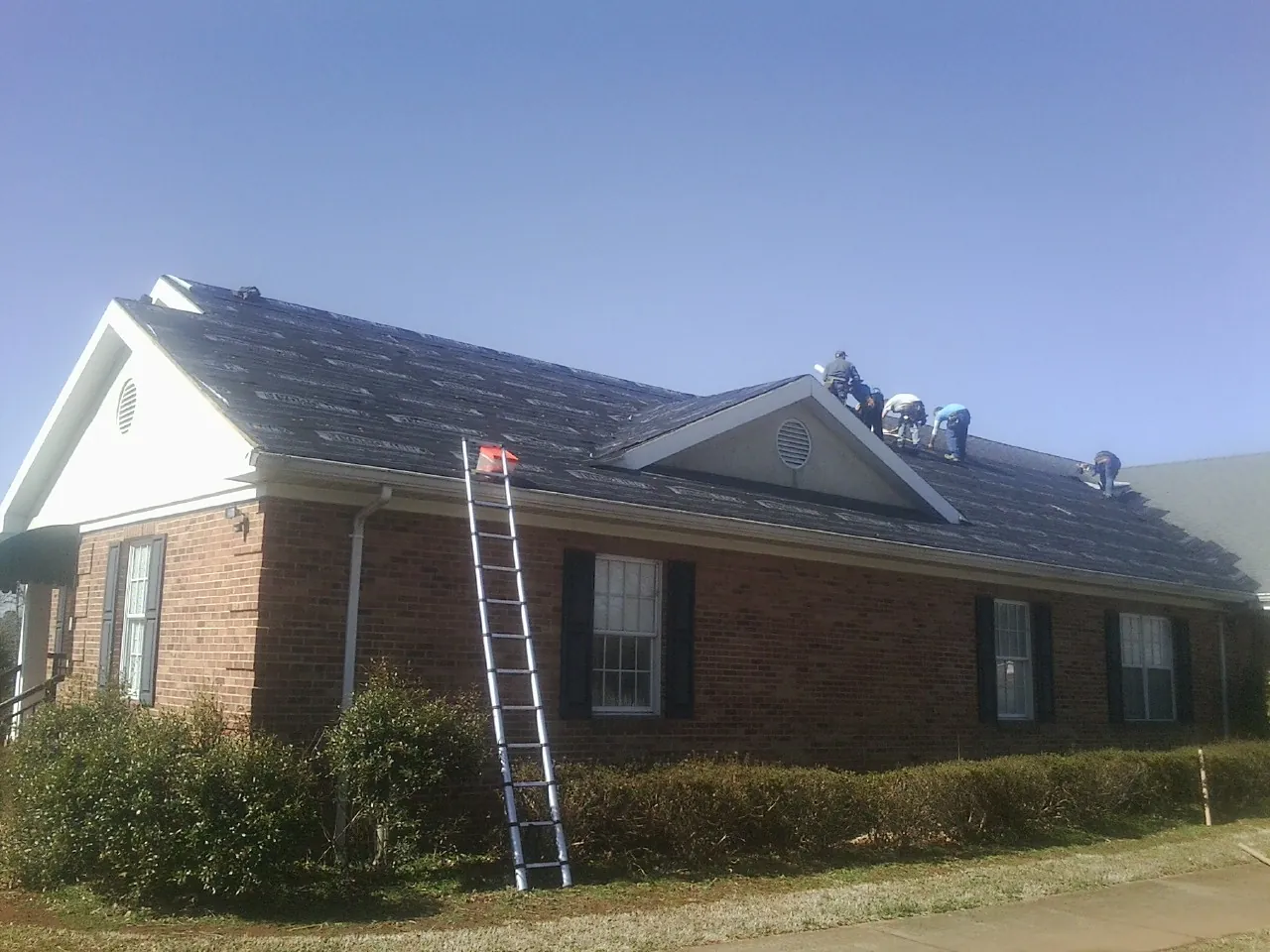 Crew tearing shingles off a brick ranch roof with a ladder set — Metal Roof Repair work by our crew in Saint Anthony
