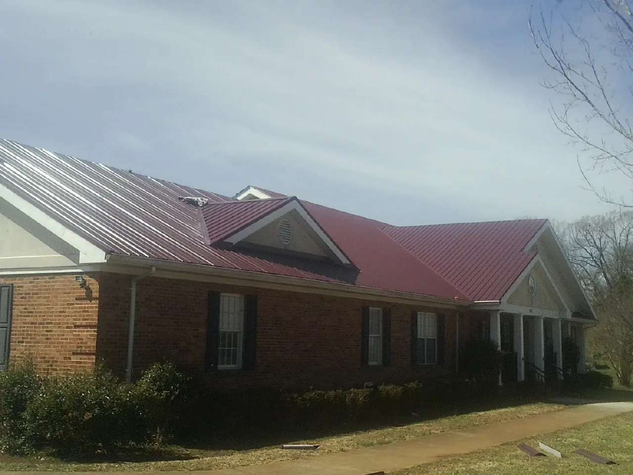 Red metal roof with gabled entries on a long brick building, from a Hail Damage Roof Repair job in Saint Anthony