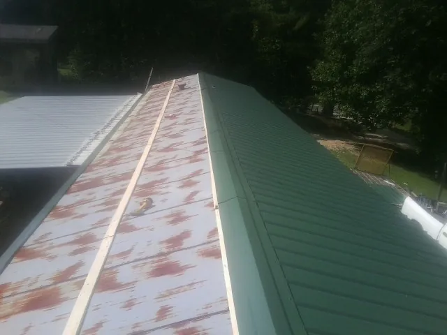 Old rusted panels beside newly installed green metal roofing in Saint Anthony