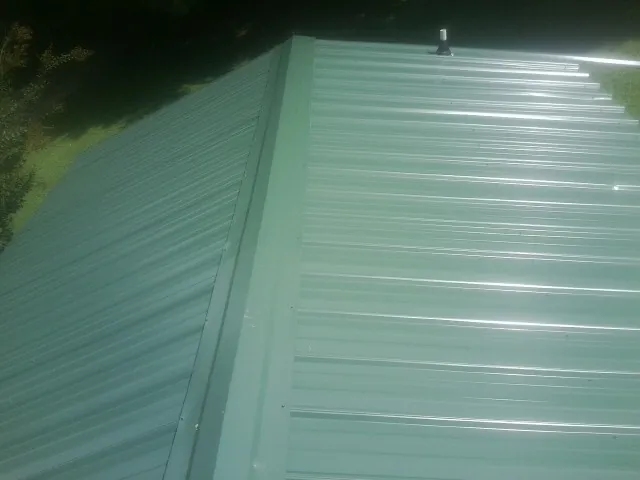 New green metal panels meeting at the ridge of a roof — Flat Roof Repair work by our crew in Saint Anthony